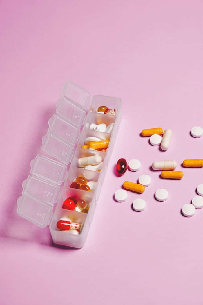 Colorful assortment of pills and capsules in organizer on pink backdrop.