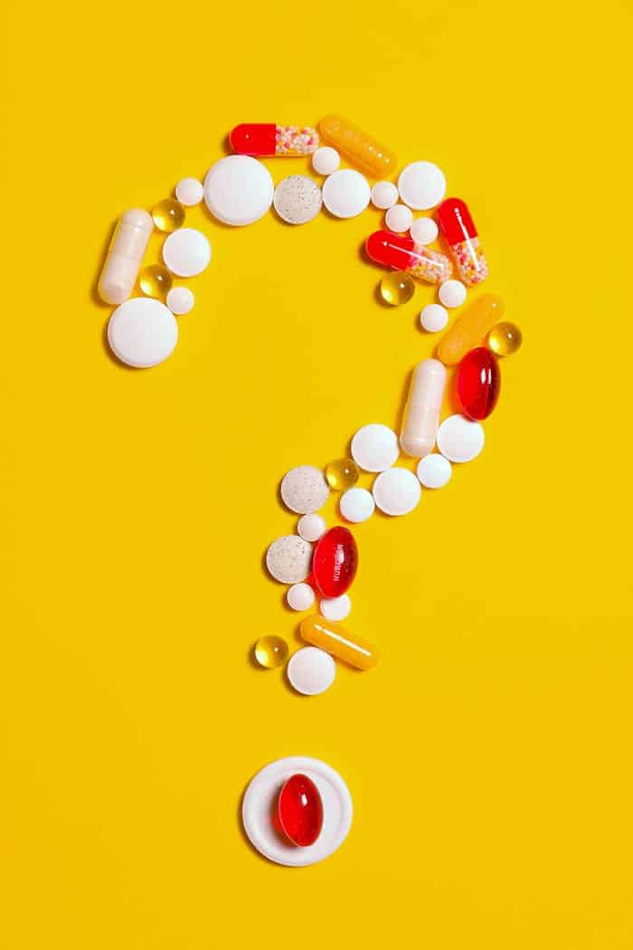 A creative arrangement of various pills forming a question mark against a bright yellow background.